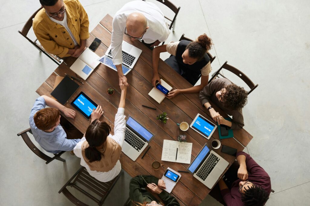 Your Solution Top view of a diverse team collaborating in an office setting with laptops and tablets, promoting cooperation.