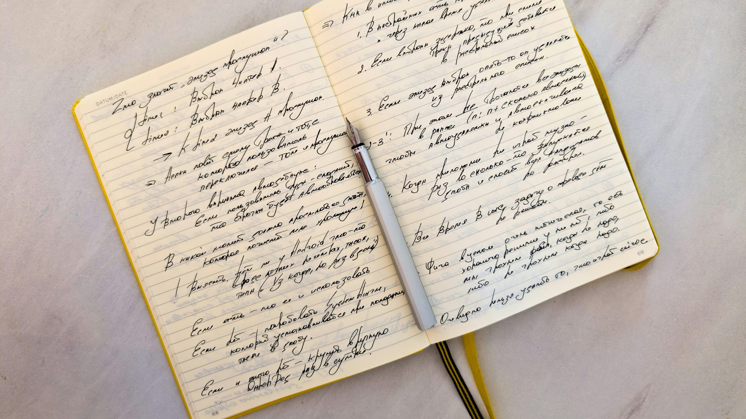 Open notebook with cursive handwritten notes on marble surface and a pen resting on pages.