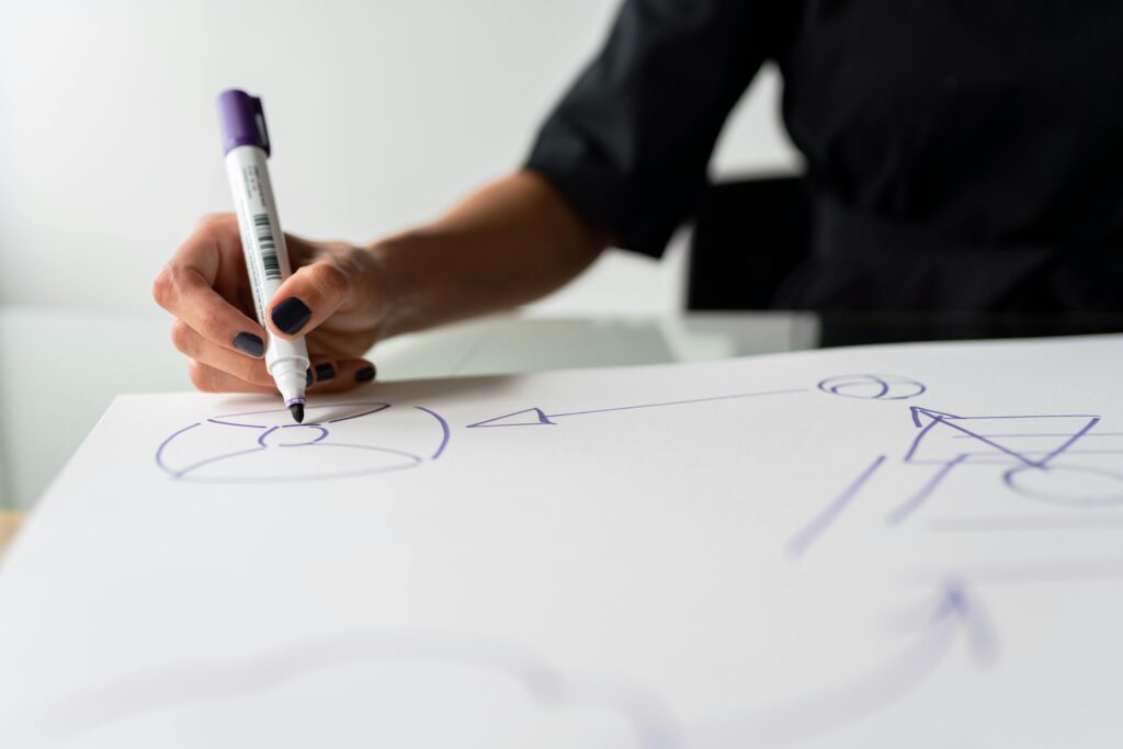 A focused view of a hand drawing with a marker on a paper, capturing creative planning in progress.